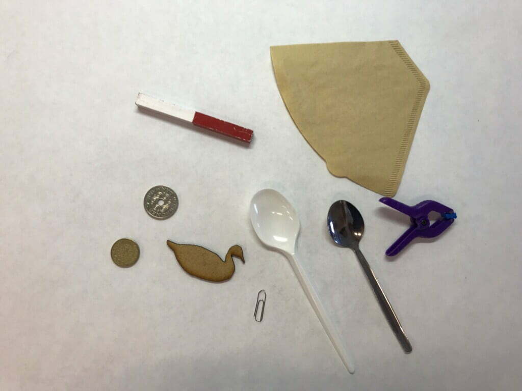 Mønter, papirklips, skeer, kaffefilter, plastik tøjklemme, småkage og magnet på et bord